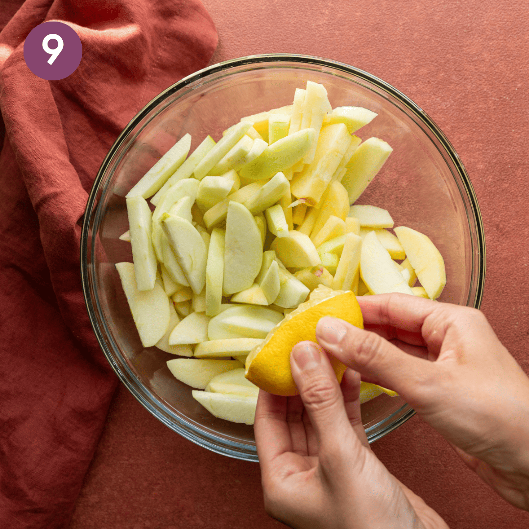 woman's hands squeezing lemon juice into sliced apples in a glass bowl.