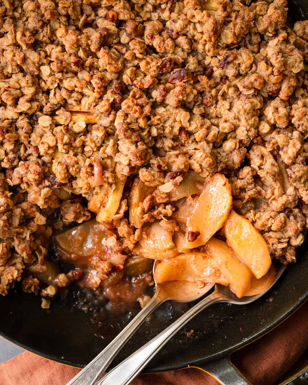 Two spoons in skillet of apple crisp on a table.
